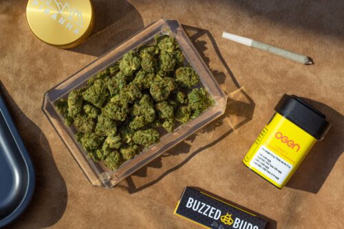 A tray of high quality cannabis bud next to a joint and a grinder.
