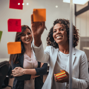 Business women looking at stickynotes stuck to glass panel during meeting