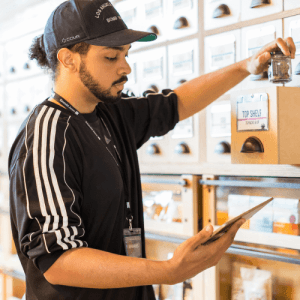 Male budtender with tablet in one hand inspecting inventory. In other hand, a glass jar of cannabis flower.