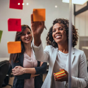 Business women looking at stickynotes stuck to glass panel during meeting